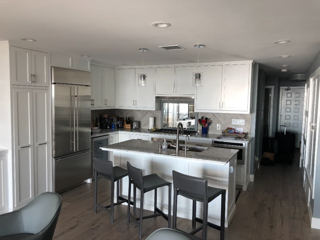 Open-concept kitchen remodel with white shaker cabinets, a stone-countered waterfall island, glass pendants, and stainless built-in refrigeration.