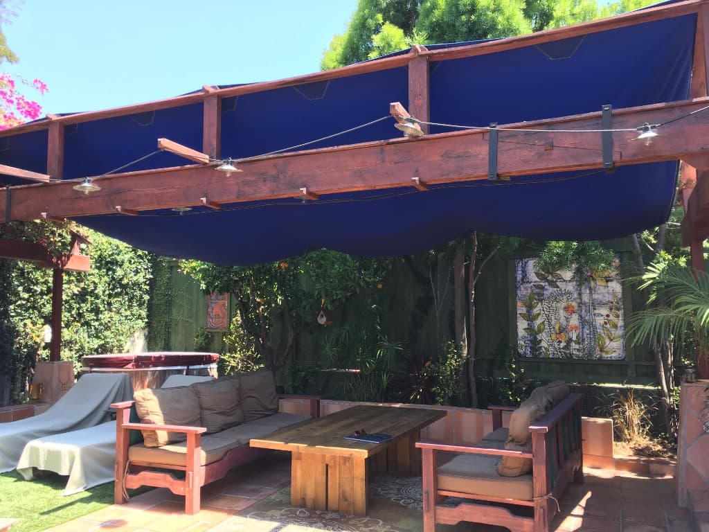 Custom redwood pergola with a deep blue shade canopy, string lights, and built-in lounge seating around a heavy-timber coffee table.